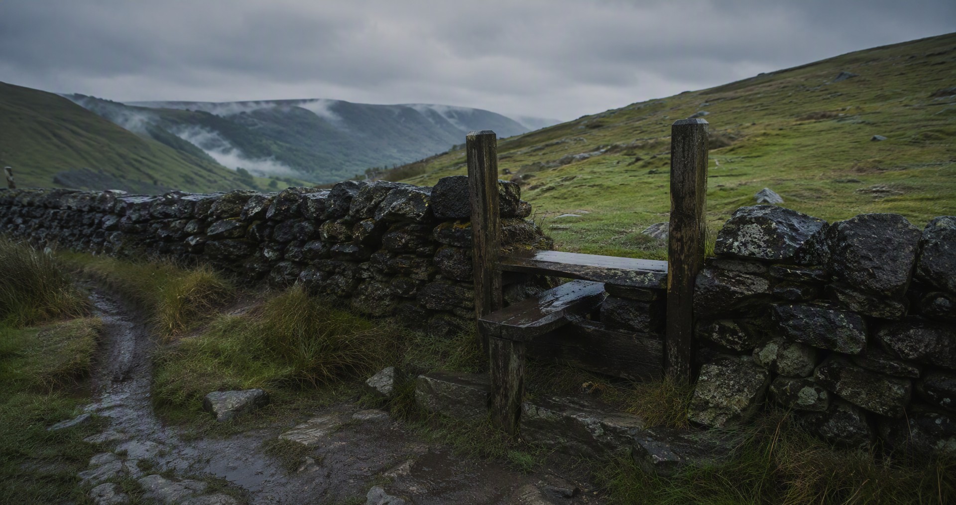 Illustrative image: a stone stile on a wet hillside path under grey skies